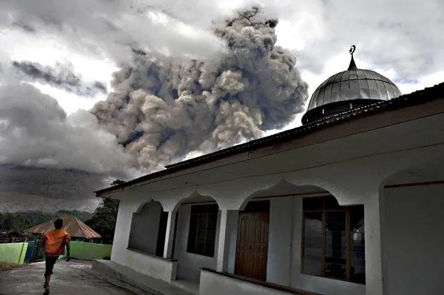 An Indonesian man stands next to a mosque in the village of Tiga Serangkai in Karo, North Sumatra on September 23, 2015, as mount Sinabung spews volcanic ash in the distance. Sinabung is one of 129 active volcanoes in Indonesia, which sits on the Pacific Ring of Fire, a belt of seismic activity running around the basin of the Pacific Ocean. (Photo by Albert Damanik/AFP Photo)