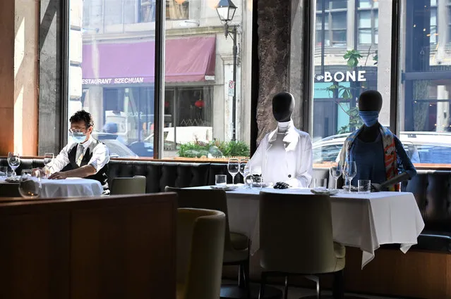 A server (L) wearing a facemask adjusts glasses on a table next to mannequins placed at a table to provide social distancing at a restaurant in old Montreal on July 10, 2020 amid the novel coronavirus pandemic. In one Montreal restaurant, patrons are getting a fashion-food two-for-one: Mannequins placed at tables not only ensure social distancing but also sport chic outfits that can be purchased to benefit charity. (Photo by Eric Thomas/AFP Photo)