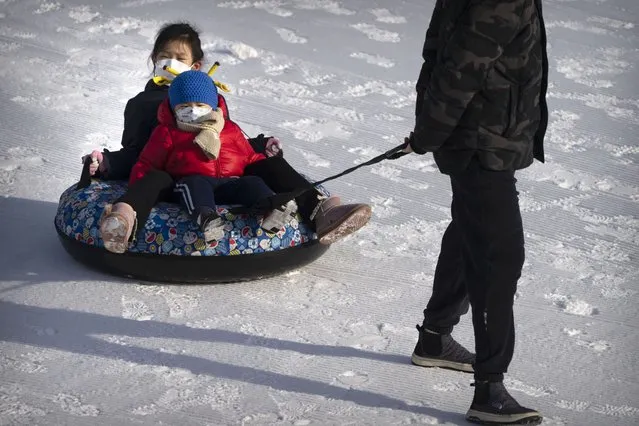 Children wearing face masks are pulled on an inner tube across the snow at an ice carnival at a public park in Beijing on the first day of the Lunar New Year holiday, Sunday, January 22, 2023. (Photo by Mark Schiefelbein/AP Photo)