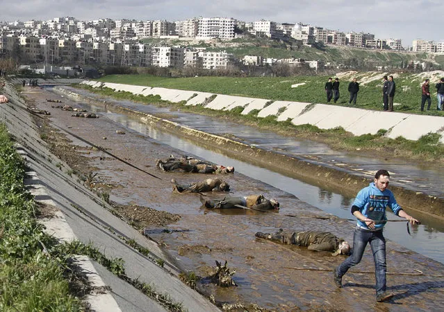 In this January 29, 2013, file photo, a man walks past dead bodies in front of a river in the neighborhood of Bustan al-Qasr in Aleppo, Syria. More than 130,000 people have died in three years, and more than a quarter of the country's population now live as refugees, either displaced internally or in neighboring countries. An untold number of people have been subjected to the trauma of losing loved ones or witnessing lives blown apart. (Photo by Abdullah al-Yassin/AP Photo)