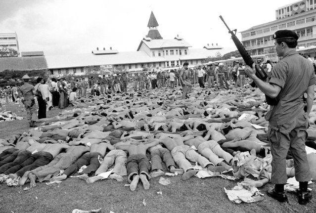 In this October 6, 1976 file photo, police stand guard over leftist Thai students on a soccer field at Thammasat University, in Bangkok, Thailand. (Photo by Gary Mangkorn/AP Photo)