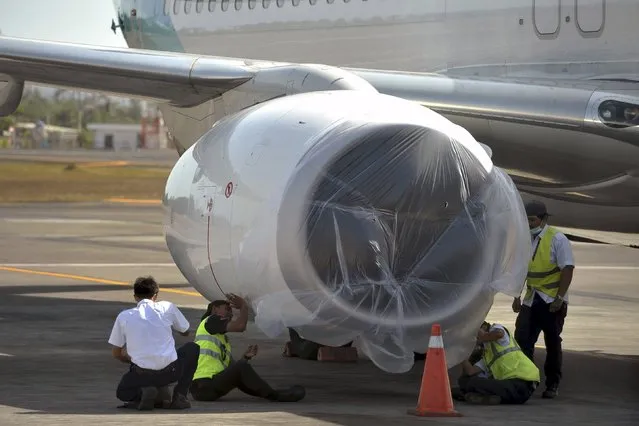 Airport workers protect an aircraft's engine with plastic at Ngurah Rai Airport on the Indonesian resort island of Bali November 4, 2015, in this photo taken by Antara Foto. Indonesia has closed Bali airport, one of its busiest international terminals, cancelling hundreds of flights, because of ash spewed by a volcano on a nearby island, authorities said on Wednesday. The resort island's Ngurah Rai airport will be closed until Thursday morning and will reopen after a re-evaluation of the situation, officials said. (Photo by Nyoman Budhiana/Reuters/Antara Foto)