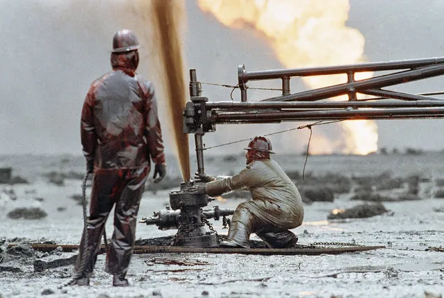 Brian Krause, of the Red Adair Co., guides an oil well capping device into place over a spouting well head as co-worker Bert Ballard looks on, Saturday, March 30, 1991 in Kuwait. The Adair Co. managed to cap the well after two attempts, plugging the hole with a mixture of mud and cement. This well was not ablaze. (Photo by Greg Gibson/AP Photo)