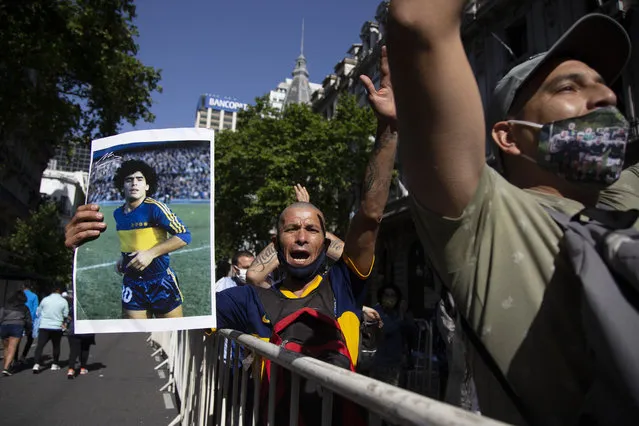 A man holds a poster of Diego Maradona when he played for the soccer club Boca Juniors, as he waits in a line outside the presidential palace to pay his last respects, in Buenos Aires, Argentina, Thursday, November 26, 2020. The Argentine soccer great who was among the best players ever and who led his country to the 1986 World Cup title died from a heart attack at his home Wednesday, at the age of 60. (Photo by Maria Paula Avila/AP Photo)