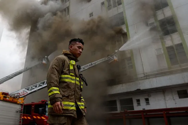 A firefighter walks next to a blaze at a warehouse in the city's bustling Kowloon district, in Hong Kong, China on March 24, 2023. (Photo by Tyrone Siu/Reuters)