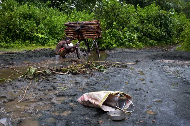 In this September 10, 2014 photo, a man washes his bicycle sitting on loose asbestos sediments brought down by a stream from Roro hills in Roro, India. (Photo by Saurabh Das/AP Photo)