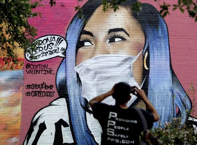 A man photographs a mural of Cardi B that was updated by the artist Colton Valentine to include a face mask to reflect the coronavirus pandemic, in San Antonio, Monday, March 30, 2020. Due to the COVID-19 outbreak, San Antonio an many other Texas cities are under stay-at-home orders. (Photo by Eric Gay/AP Photo)