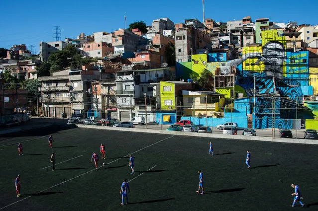 Residents play football in a field with the image of Brazilian football player Gabriel Jesus in the background, painted on the walls of houses in the Perus neighbourhood, were he lived during his childhood in the outskirts of Sao Paulo, Brazil on May 20, 2018. (Photo by Nelson Almeida/AFP Photo)