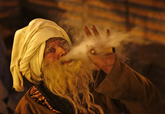 A Sadhu or Hindu holy man smokes marijuana at “Sangam”, the confluence of holy rivers of Ganges, Yamuna and the mythical Saraswati, during the annual traditional fair of Magh Mela in Allahabad, in the northern Indian state of Uttar Pradesh, India, Thursday, January 15, 2015. Hundreds of thousands of devout Hindus are expected to take holy dips at the confluence during the astronomically auspicious period of over 45 days celebrated as Magh Mela. (Photo by Rajesh Kumar Singh/AP Photo)