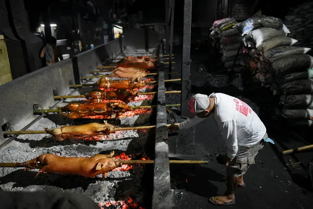 A worker roasts a row of pigs on bamboo poles at a roasting pit, in Manila, Philippines, December 21, 2020. (Photo by Lisa Marie David/Reuters)