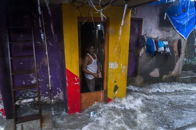 An Indian man stands at the door of his house as waves caused by high tide hits the huts on the shore of the Arabian Sea in Mumbai, India, Thursday, July 6, 2023. (Photo by Rafiq Maqbool/AP Photo)