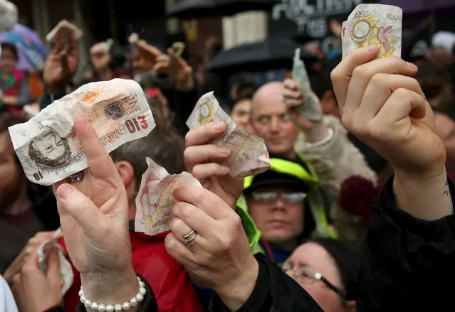 People hold out money as butchers sell their remaining produce of the year at discounted prices during the traditional Christmas Eve auction at Smithfield's market in London December 24, 2015. (Photo by Neil Hall/Reuters)