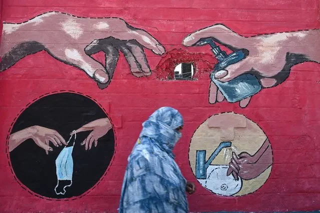 A pedestrian walks past a mural of Michelangelo's fresco painting the “Creation of Adam”, depicting a hand with a hand soap bottle, to spread awareness about the COVID-19 coronavirus, in Mumbai on March 31, 2021. (Photo by Indranil Mukherjee/AFP Photo)