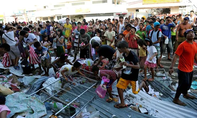 Residents watch as others throw goods from a warehouse in Guiuan,  Eastern Samar province, central Philippines Monday, November 11, 2013, after Typhoon Haiyan devastated the town on November 8. Typhoon-ravaged Philippine islands faced an unimaginably huge recovery effort that had barely begun Monday, as bloated bodies lay uncollected and uncounted in the streets and survivors pleaded for food, water and medicine. (Photo by Ted Aljibe/AP Photo)