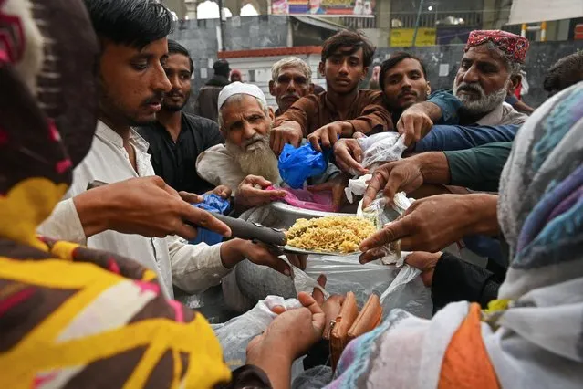 People gather along the roadside to receive free food being distributed on the occasion of World Food Day in Lahore on October 16, 2023. (Photo by Arif Ali/AFP Photo)