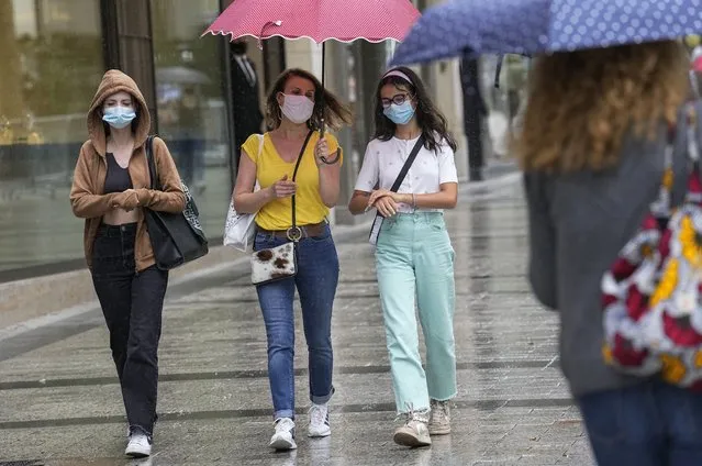People wearing a face masks to protect against coronavirus walk along the Champs Elysees avenue in Paris, Monday, July 12, 2021. France's President Emmanuel Macron is hosting a top-level virus security meeting Monday morning and then giving a televised speech Monday evening, the kind of solemn speech he's given at each turning point in France's virus epidemic. (Photo by Michel Euler/AP Photo)