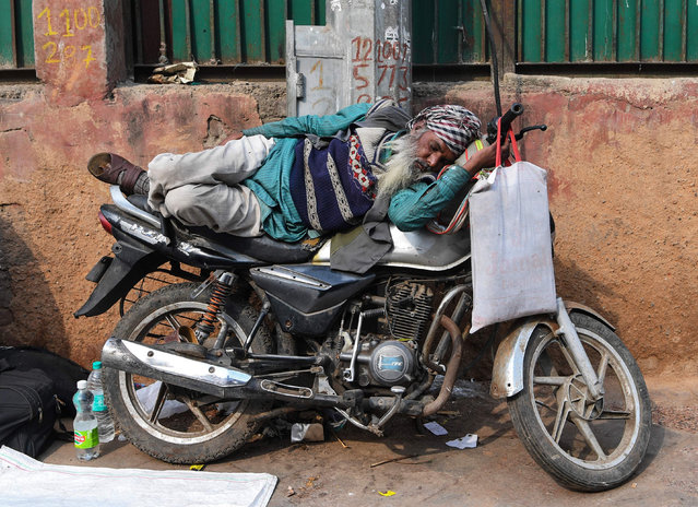 An Indian man sleeps on a motorbike in the old quarters of New Delhi on January 30, 2019. (Photo by Sajjad Hussain/AFP Photo)