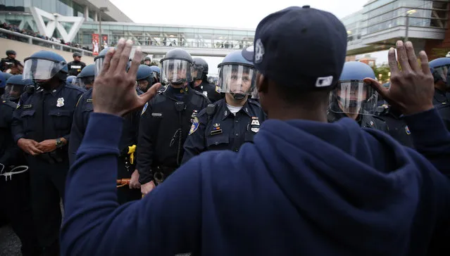 A man holds his hands up in front of a line of helmeted police after a march to City Hall for Freddie Gray, Saturday, April 25, 2015 in Baltimore. (Photo by Alex Brandon/AP Photo)