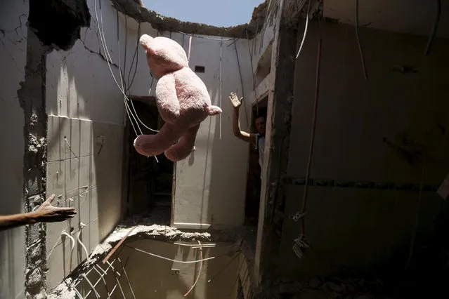A worker throws a stuffed toy to another as they move furniture from a house damaged after an air strike by a Saudi-led coalition struck a nearby missile base, in Yemen's capital Sanaa, April 23, 2015. (Photo by Khaled Abdullah/Reuters)