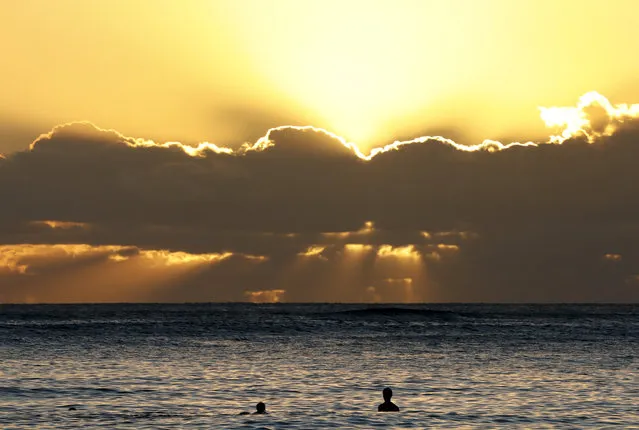 Swimmers watch the sun set behind clouds over the Pacific Ocean seen from Waikiki Beach in Honolulu, Hawaii, Saturday, December 31, 2016, the last sunset of 2016. (Photo by Carolyn Kaster/AP Photo)