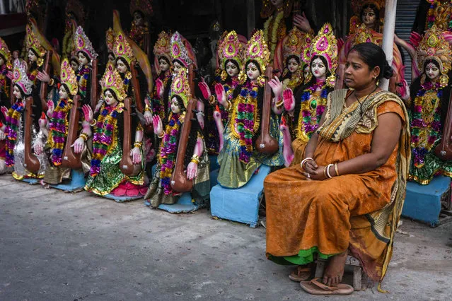 A vendor sits on a roadside stall with clay idols of Hindu goddess of knowledge, Saraswati, as she awaits  customers on the eve of its worship on the auspicious day of Vasant Panchami, in Kolkata, India, Tuesday, February 13, 2024. (Photo by Bikas Das/AP Photo)