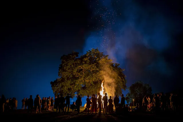 People stand around a bonfire during a celebration of Saint John's Day and Summer solstice at the small town of Kernave, some 35km (74,5 miles) northwest of the capital Vilnius, Lithuania, Thursday, June 24, 2021. St. John's Day or Midsummer Day, shortest night of the year, is filled with magic – the festivities include making oak leaf wreaths and leaping over flames, and young people are encouraged to go out and look for fern flowers. (Photo by Mindaugas Kulbis/AP Photo)