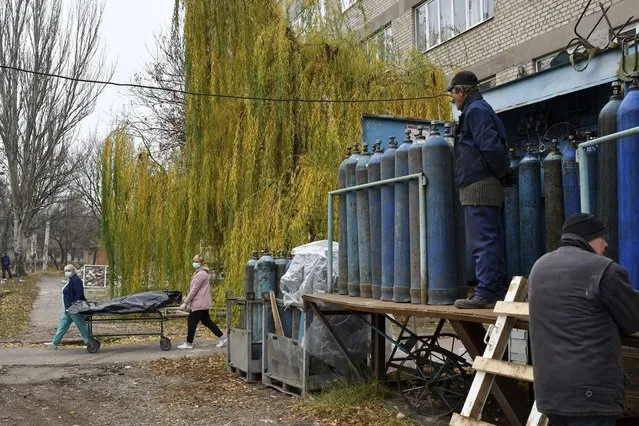 Workers stand by oxygen tanks for an ICU as medical staff carry a body of a patient who died of coronavirus on a stretcher, at the morgue of a hospital in Kramatorsk, Ukraine, Saturday, November 6, 2021. Ukraine's health ministry has reported a one-day record of 793 deaths from COVID-19. Ukraine has been inundated by coronavirus infections in recent weeks, putting the country's underfunded medical system under severe strain. (Photo by Andriy Andriyenko/AP Photo)