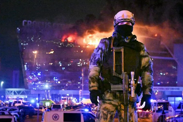 A Russian Rosguardia (National Guard) servicemen secures an area as a massive blaze seen over the Crocus City Hall on the western edge of Moscow, Russia, Friday, March 22, 2024. Several gunmen have burst into a big concert hall in Moscow and fired automatic weapons at the crowd, injuring an unspecified number of people and setting a massive blaze in an apparent terror attack days after President Vladimir Putin cemented his grip on the country in a highly orchestrated electoral landslide. (Photo by Dmitry Serebryakov/AP Photo)