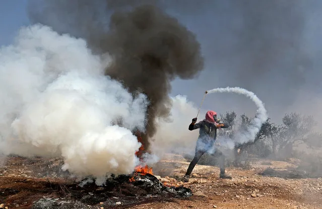 A Palestinian protester uses a slingshot to return a tear gas canister toward Israeli security forces during clashes following a demonstration against settlements in the village of Beita in the occupied West Bank, on October 8, 2021. (Photo by Jaafar Ashtiyeh/AFP Photo)