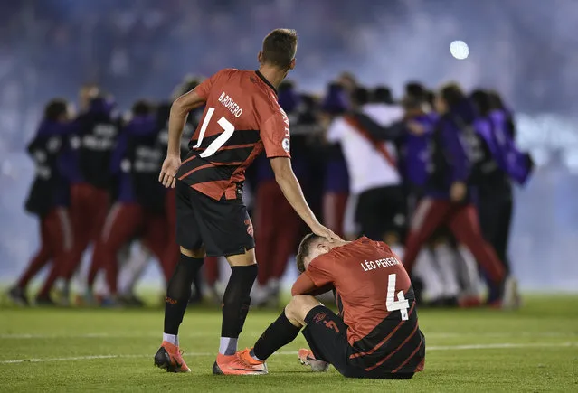 Leo Pereira of Brazil's Athletico Paranaense sits on the field as teammate Braian Romero pats him on the head after they lost the Recopa Sudamericana final soccer match 3-0 to Argentina's River Plate, celebrating behind, in Buenos Aires, Argentina, Thursday, May 30, 2019. (Photo by Gustavo Garello/AP Photo)