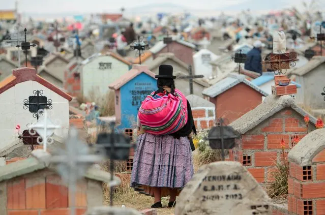A woman stands among graves at the Mercedario graveyard as she observes the Day of the Dead celebration, in El Alto, on the outskirts of La Paz, Bolivia, November 2, 2021. (Photo by Manuel Claure/Reuters)