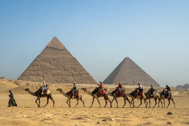 A guide pulls a lead camel as tourists ride in a row past the Great Pyramid of Khufu (Cheops, R) and the Pyramid of Khafre (Chephren, L) at the Giza Pyramids Necropolis on the outskirts of Giza on May 3, 2024. (Photo by Jewel Samad/AFP Photo)