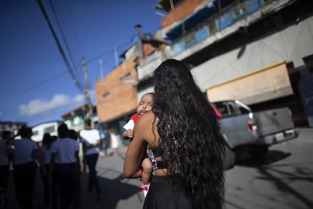 In this photo taken July 25, 2019, 15-year-old Nicol Ramirez carries her baby girl to a lab where she will pay to get a pregnancy test, a prerequisite for a hormonal implant to prevent future pregnancies, of which there is a very limited number, in the Caucaguita neighborhood on the outskirts of Caracas, Venezuela. With condoms and birth control pills either impossible to find or too expensive, Ramírez found out she was pregnant at 14 with her boyfriend, who responded coldly to her pregnancy and hasn't heard from him since. (Photo by Ariana Cubillos/AP Photo)