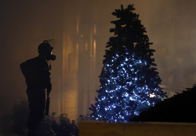 A riot police officer stands next of a Christmas tree during a protest where some anti-government protesters try to enter parliament square in downtown Beirut, Lebanon, Saturday, December 14, 2019. (Photo by Hussein Malla/AP Photo)