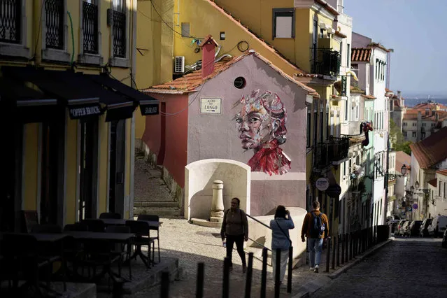 A woman takes pictures of street art in Lisbon, Tuesday, April 19, 2022. (Photo by Armando Franca/AP Photo)