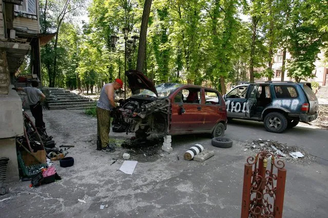 A man repairs a car in a residential area of Mariupol on June 1, 2022, amid the ongoing Russian military action in Ukraine. (Photo by AFP Photo/Stringer)