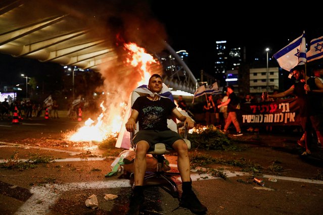 A protester sits as fire emerges during a demonstration against Israeli Prime Minister Benjamin Netanyahu and his nationalist coalition government's judicial overhaul, in Tel Aviv, Israel on July 20, 2023. (Photo by Corinna Kern/Reuters)