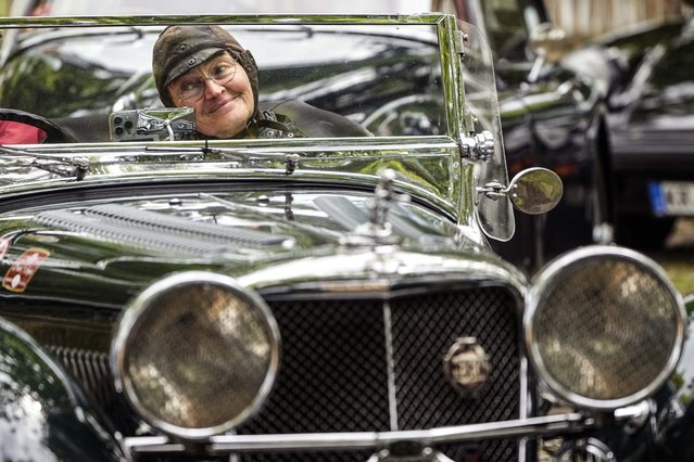 A woman checks her outfit with a smartphone on the dashboard, sitting in her vintage car at a classic car meeting in Duesseldorf, Germany, Friday, August 4, 2023. (Photo by Martin Meissner/AP Photo)