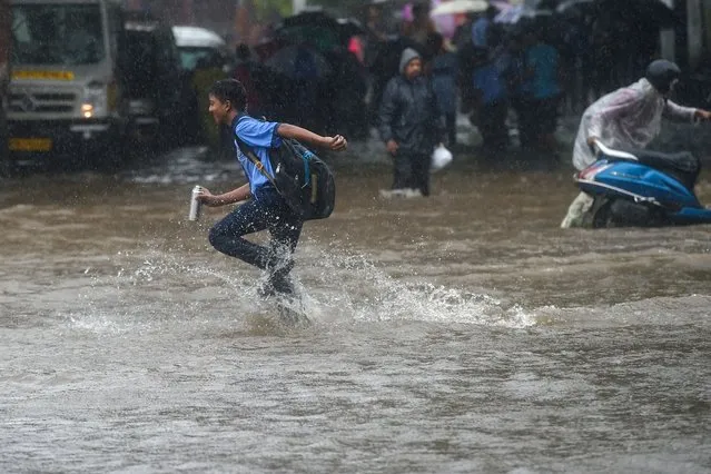 A school boy runs through a flooded street during rain showers in Mumbai on July 5, 2022. (Photo by Punit Paranjpe/AFP Photo)
