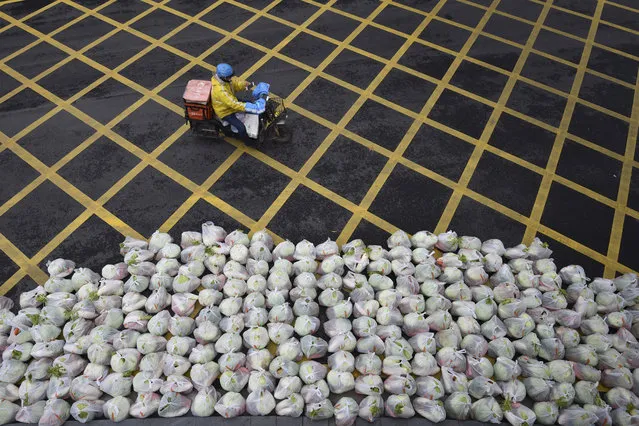 A man rides past bags of vegetables being prepared for delivery on an almost empty street in Wuhan, in China's central Hubei province on February 26, 2020. China on February 26 reported 52 new coronavirus deaths, the lowest figure in more than three weeks, bringing the death toll to 2,715. All the new deaths were in the outbreak epicentre Hubei province, which accounted for 401 of the 406 new infections reported on February 26, the National Health Commission said. (Photo by AFP Photo/China Stringer Network)