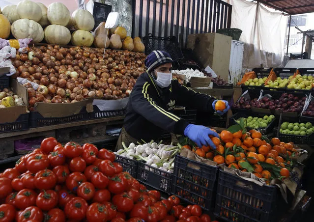 Syrian Sami Jawabreh wears a mask and gloves, as he rearranges fruits on display for sale at his shop, in Beirut, Lebanon, Wednesday, March 18, 2020. Lebanon has been taking strict measures to limit the spread of the coronavirus closing restaurants and nightclubs as well as schools and universities. For most people, the new coronavirus causes only mild or moderate symptoms. For some it can cause more severe illness. (Photo by Bilal Hussein/AP Photo)