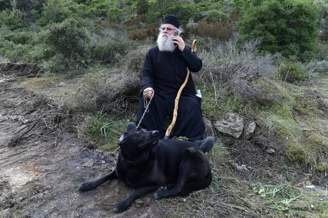 A Greek Orthodox priest speaks on his cellphone as he holds a dog at a roadblock in Karava, on the northeastern Aegean island of Lesbos, Greece, Thursday, February 27, 2020. Greece's government hoped to defuse tensions after protests over plans for new migrant camps on two of its islands Wednesday turned into violent clashes between police and local residents, some armed with Molotov cocktails and shotguns. (Photo by Michael Varaklas/AP Photo)