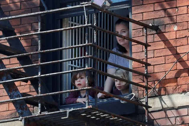 A woman and children look out a window from an apartment in Greenwich Village in Manhattan during the outbreak of the coronavirus disease (COVID-19) in New York City, New York, U.S., March 26, 2020. (Photo by Mike Segar/Reuters)