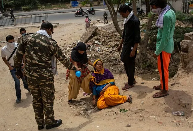 A woman is helped by her daughter and a paramilitary soldier after she fainted on her way to home from a bank, during a nationwide lockdown to slow the spreading of the coronavirus disease (COVID-19), in New Delhi, April 14, 2020. (Photo by Danish Siddiqui/Reuters)