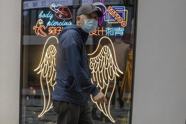A man wearing a mask against the coronavirus walks past neon signs for a tattoo shop in Beijing Friday, May 8, 2020. China and South Korea both reported more coronavirus infections Friday after reopening economies damaged by devastating outbreaks. Around the globe, governments are opting to accept the risks of easing pandemic-fighting restrictions that left huge numbers of people without income or safety nets. (Photo by Ng Han Guan/AP Photo)