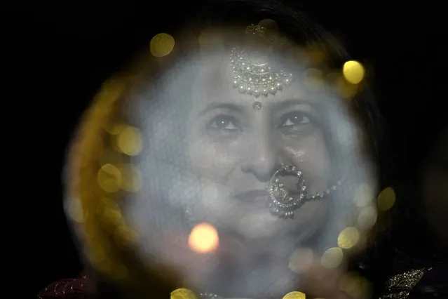 A married Hindu woman looks at the moon through a sieve as part of a ritual to break her fast during Karva Chauth festival in Jammu, India, Thursday, October 13, 2022. Hindu married women decorate their hands with henna, wear colorful bangles and observe a fast to pray for the longevity and well being of their husbands during this festival. (Photo by Channi Anand/AP Photo)