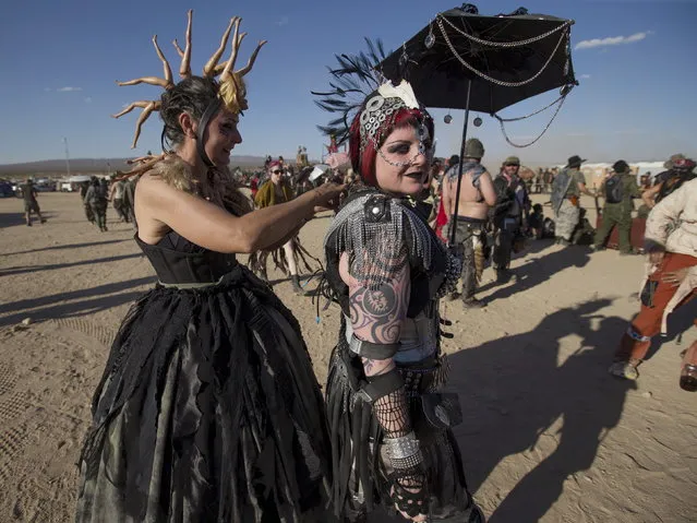 Barbara Ellquist (L) helps fellow enthusiast Christine Shea with her costume during the Wasteland Weekend event in California City, California September 26, 2015. (Photo by Mario Anzuoni/Reuters)