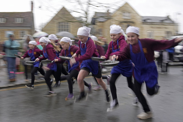 Schoolchildren from local schools take part in the children's races prior to the annual Pancake race in the town of Olney, in Buckinghamshire, England, Tuesday, February 13, 2024. Every year women clad in aprons and head scarves from Olney and the city of Liberal, in Kansas, USA, run their respective legs of the race with pancakes in their pans. According to legend, the Olney race started in 1445 when a harried housewife arrived at church on Shrove Tuesday still clutching her frying pan with a pancake in it. (Photo by Kin Cheung/AP Photo)