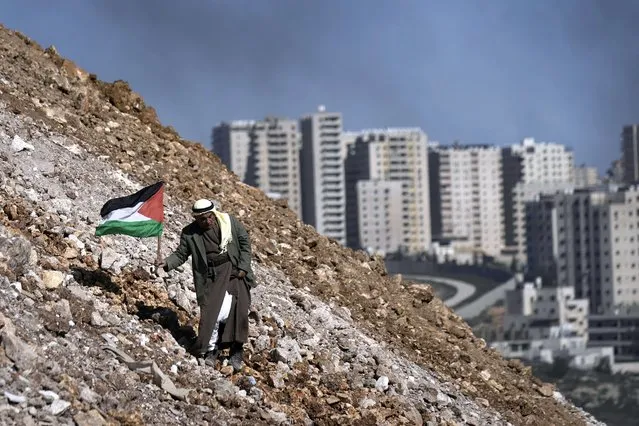 An elderly Palestinian walks with a Palestinian flag during a demonstration against a new Israeli settlement in the village of Qalandia near the West Bank city of Ramallah., Friday, January 20, 2023. (Photo by Majdi Mohammed/AP Photo)