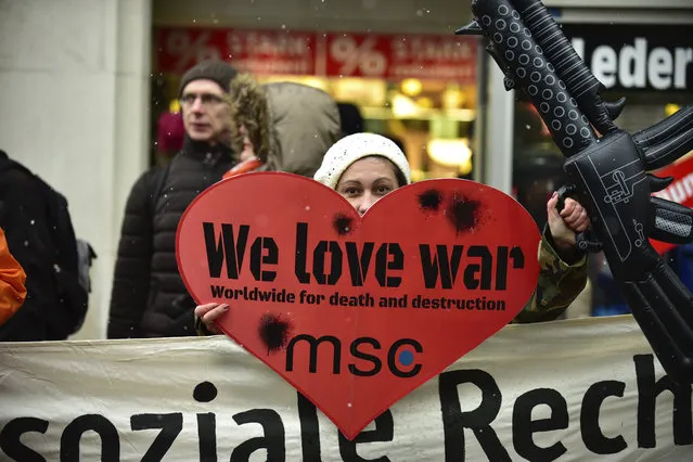 A demonstrator carries  a poster reading: “We Love War”  as they  protest against the Security Conference, MSC,  in Munich, Germany, Saturday, February 17, 2018. (Photo by Sebastian Gabriel/DPA via AP Photo)